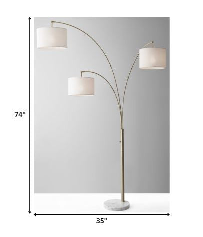 74" Brass Three Light Arc Floor Lamp With Off White Fabric Drum Shade